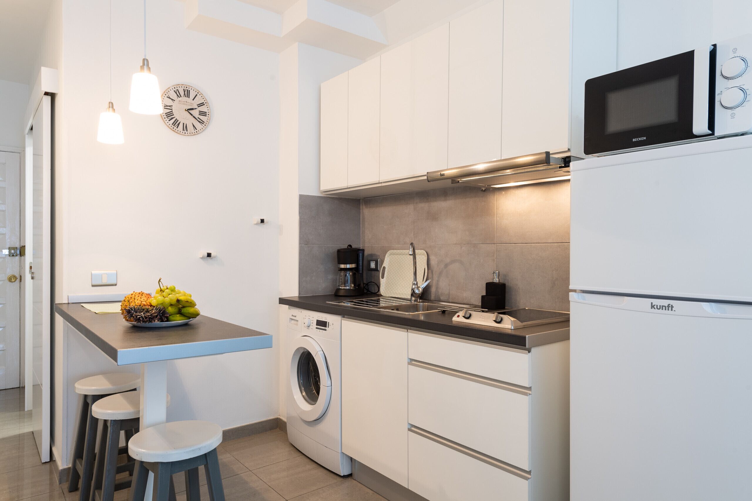 Una cocina moderna con lavadora, microondas y un frutero sobre la encimera.