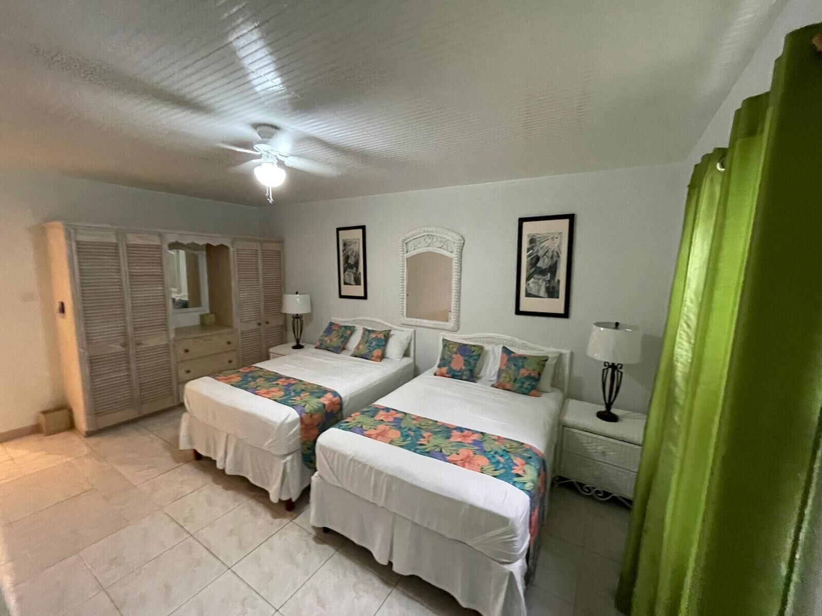 A bedroom with two beds, a ceiling fan, a wardrobe, and a green curtain.