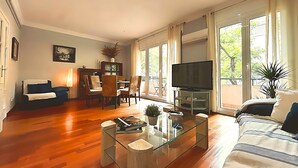 Una sala de estar con una mesa de centro de vidrio, un sofá, un televisor y un comedor con sillas y un aparador.