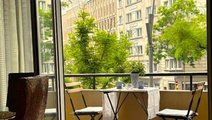 Una habitación con suelo de madera, una mesa con sillas, una planta en maceta y vistas a un balcón con mesa y sillas.