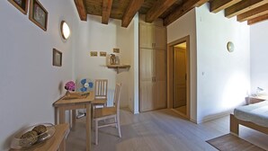 Ein Zimmer mit Holzboden, einem Esstisch mit Stühlen, einem Bett mit gemustertem Überwurf und einer Tür zu einem weiteren Raum.