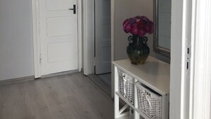 Een gang met een witte deur, een spiegel en een vaas met bloemen op een witte console.