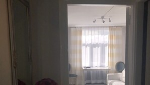 Een smalle gang die leidt naar een slaapkamer met een bed, een stoel en een tafel met een bloevas.