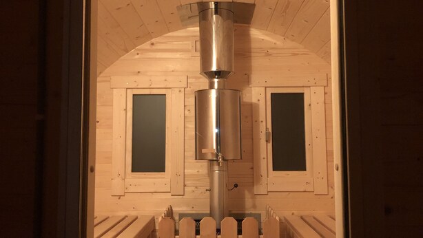 Een houten blokhut met een centrale metalen constructie, twee ramen en een houten omheining.