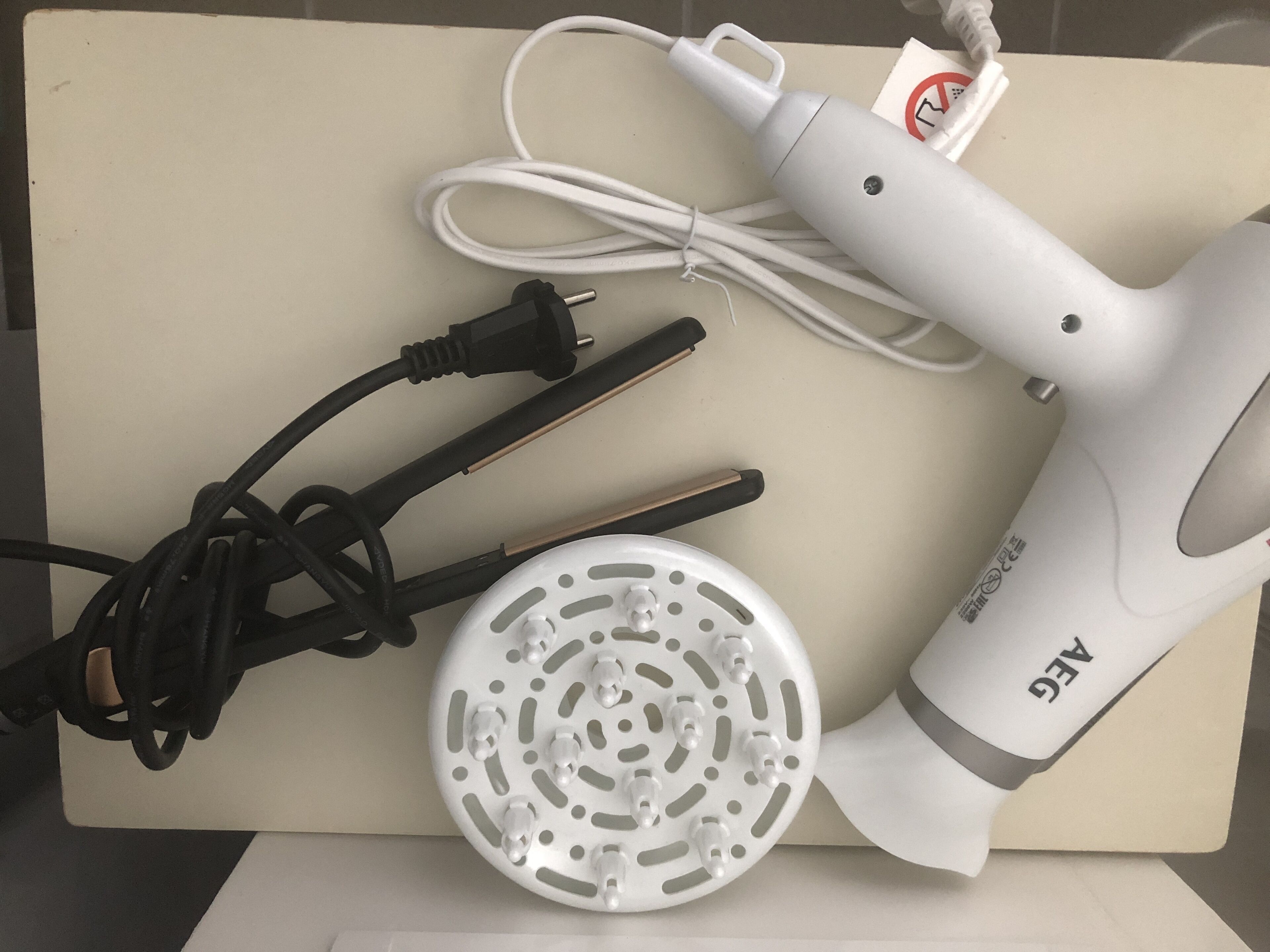 Un sèche-cheveux, son cordon d’alimentation et un adaptateur de prise électrique, le tout posé sur une surface beige.