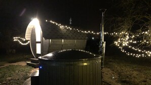 Een hottub met een houten buitenkant en een metalen dak, omringd door lichtjes.