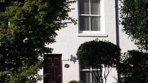 A two-story white house with a brick chimney, a wooden door, and a window with shutters. - Pretty Victorian cottage (1860) in a charming setting, 15 min walk from seafront (Portsmouth)
