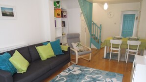 A living room with a black sofa, a blue floral rug, a wooden coffee table, a grey armchair, and a teal staircase. - Pretty Victorian cottage (1860) in a charming setting, 15 min walk from seafront (Portsmouth)