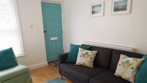 A living room with a dark brown sofa, teal cushions, a teal door, and a blue patterned rug. - Pretty Victorian cottage (1860) in a charming setting, 15 min walk from seafront (Portsmouth)
