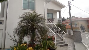 Un edificio de dos pisos con fachada blanca, un balcón en el segundo nivel y una escalera que conduce a la entrada.