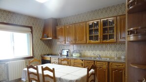 Una cocina con armarios de madera, una mesa de comedor con sillas y un ventanal con persianas.