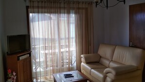 Una sala de estar con un sofá, una mesa de centro de vidrio, un televisor sobre un mueble de madera y una araña.