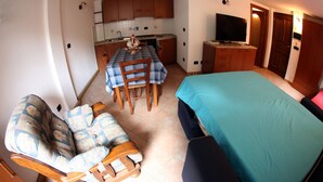 Una habitación compacta con cama, sofá, mesa de comedor y kitchenette.