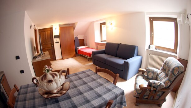 Una sala acogedora con una mesa de comedor, un sofá, un sillón mecededor y una pequeña cocina americana.