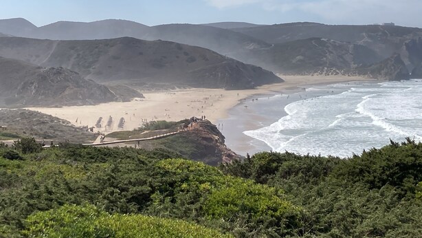 A coastal landscape with a beach, rocky cliffs, and a clear sky.