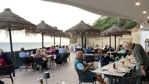 An outdoor dining area with tables and chairs, thatched umbrellas, and a view of the sea.