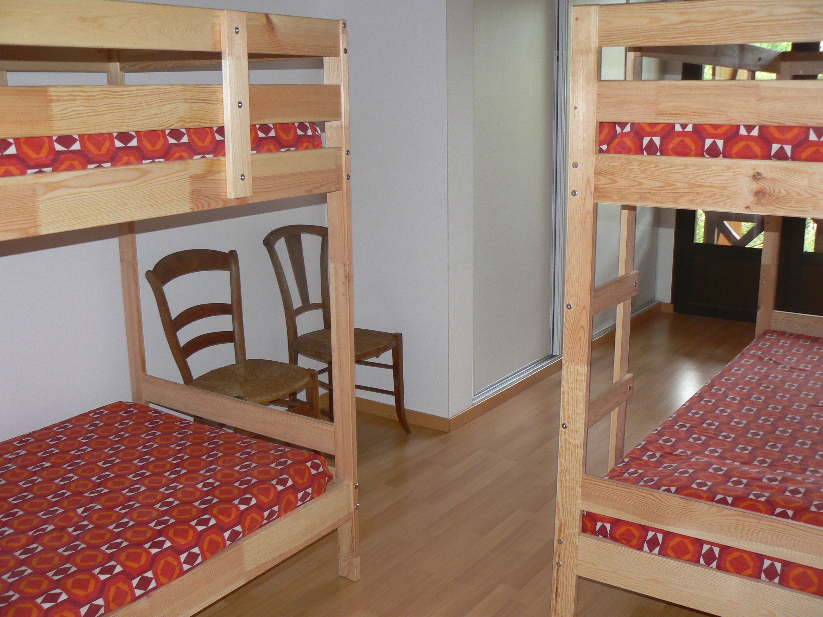 A bunk bed room with a wooden chair and a patterned bedspread.