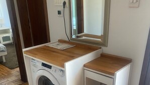 A compact, white washing machine with a wooden top and a small shelf, placed in a corner of a room with wooden flooring and a mirror above it. - Peaceful holidays for an active family (Stari Grad)