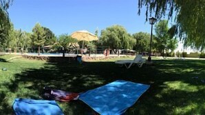 Un parc avec une piscine, des chaises longues et une personne allongée sur une couverture.