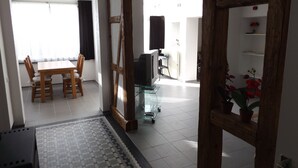 A spacious living area with a dining table and chairs, a television, and a potted plant.