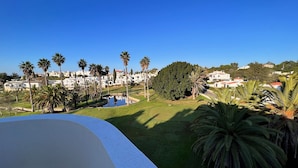 Une vue d’un quartier résidentiel avec un grand arbre, un petit étang et des maisons aux toits rouges.