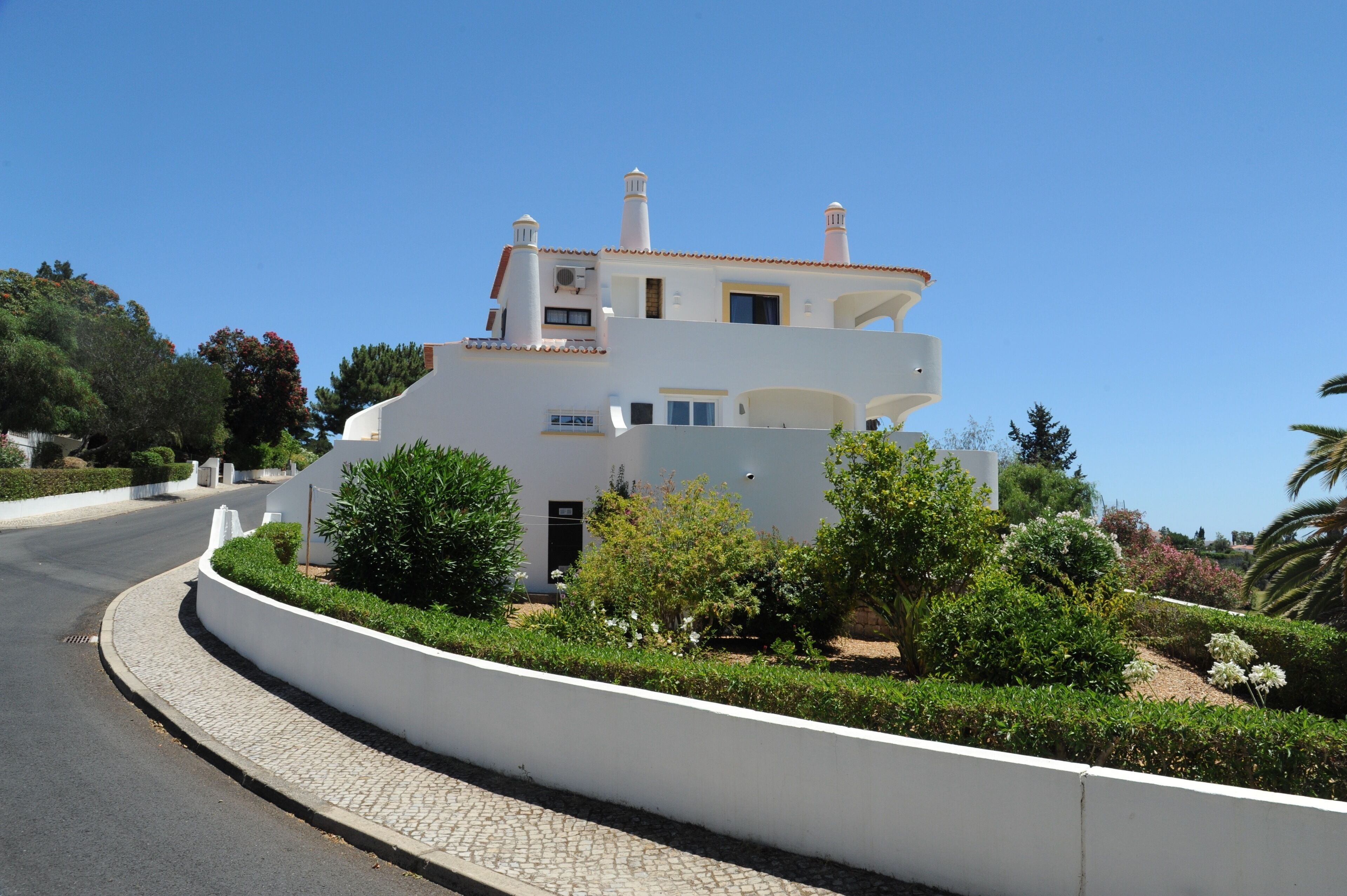 Ein modernes, zweistöckiges Haus mit einer geschwungenen Auffahrt, umgeben von gepflegten Gärten und wolkenlosem, blauem Himmel.