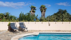Une piscine avec deux chaises longues et un mur blanc, le tout sur fond de verdure.