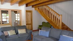 Sala de estar com dois sofás cinzas, uma mesa de centro de vidro e uma escada de madeira.