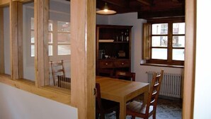 Uma área de refeições com mesa e cadeiras de madeira, uma janela com vista e uma estante de livros.