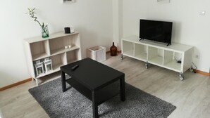 En moderne stue med et sort sofabord, et hvidt reolsystem og et fjernsyn på et hvidt tv-møbel.