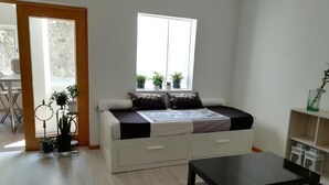 En kompakt opholdsstue med sovesofa, et lille bord og et vindue med planter.