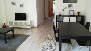 En moderne stue med et fjernsyn, et hvidt tv-møbel og et spiseområde med et sort bord og stole.