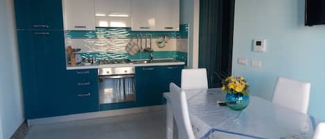 A modern kitchen with blue cabinets, a stainless steel stove, and a dining area with a table and chairs.
