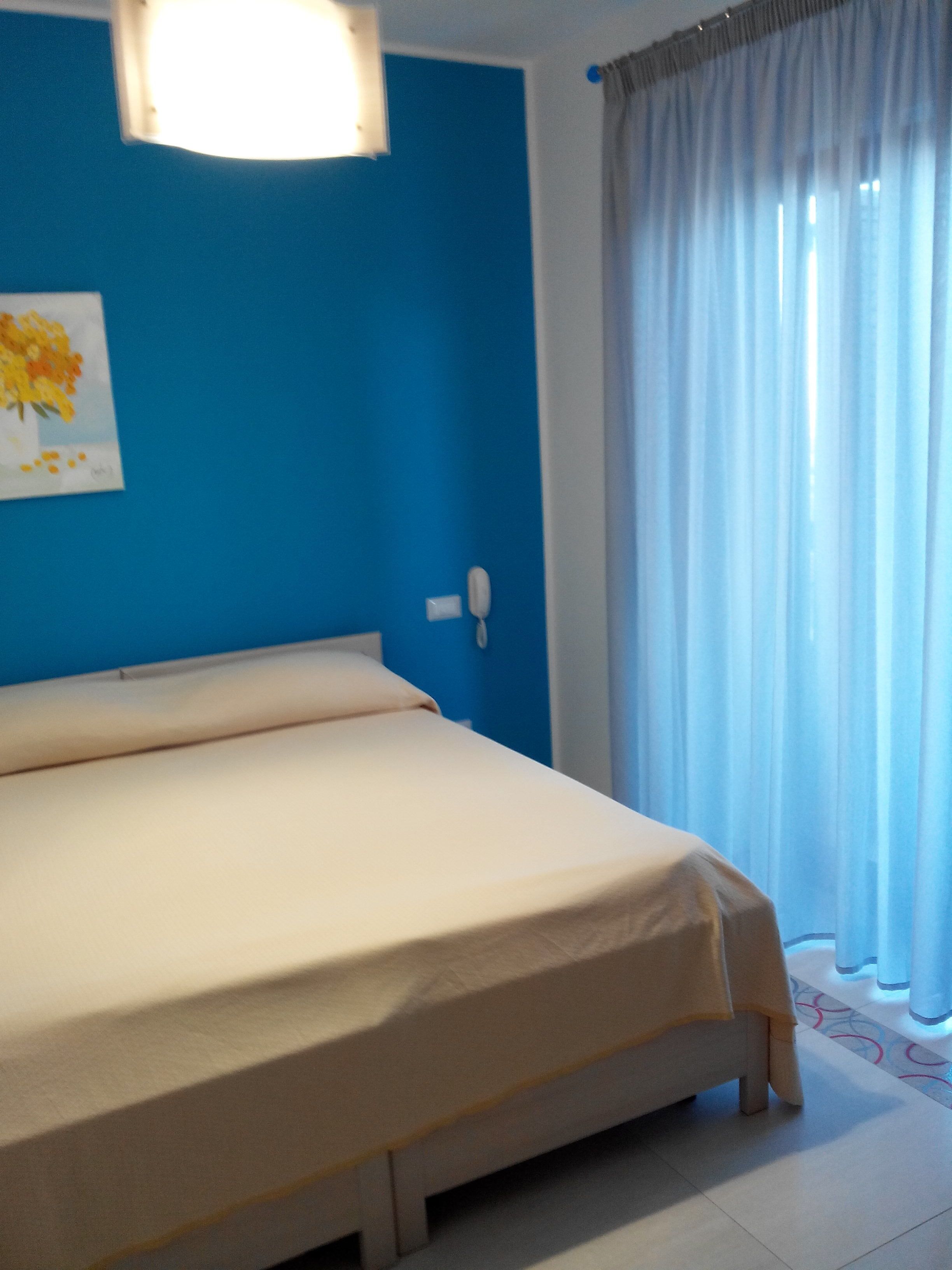 Un lit dans une chambre avec un mur bleu, un téléphone blanc et une fenêtre avec des rideaux.
