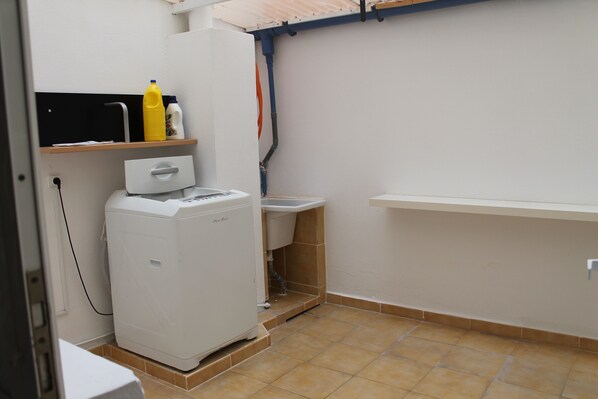 A compact laundry room with a washing machine, a sink, and a shelf with cleaning supplies.
