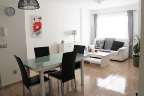 A modern living room with a glass dining table, black chairs, a white sofa, and a coffee table.