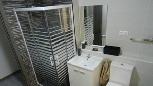 Un baño moderno con ducha de vidrio, lavabo blanco, inodoro y espejo sobre el lavabo.