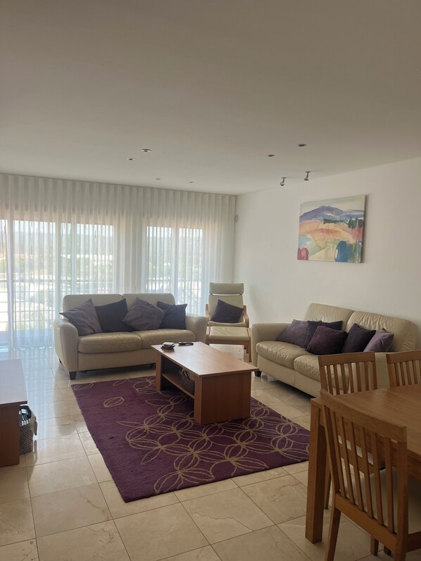 A modern living room with two beige sofas, a wooden coffee table, and a purple rug.