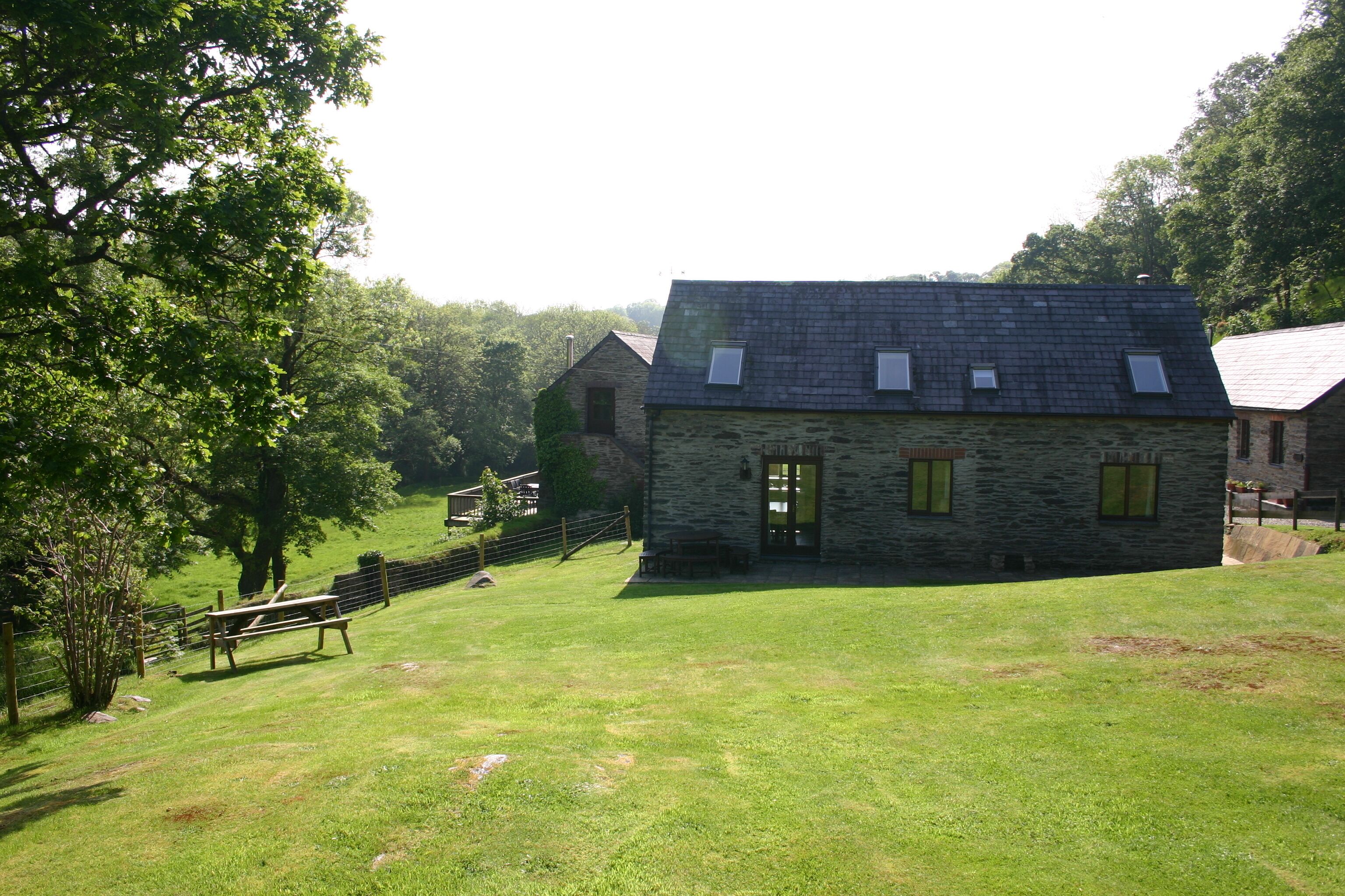 A stone building with a sloped roof, a small porch, and a grassy yard with a wooden bench.