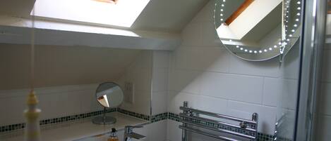 A bathroom with a skylight, a round mirror with lights, a sink, and a towel rack.