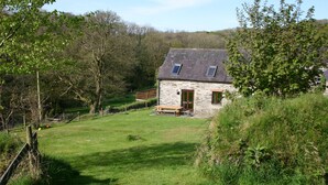 Ein Haus aus Stein mit einem geneigten Dach, einer Holzterrasse und einem Rasen.