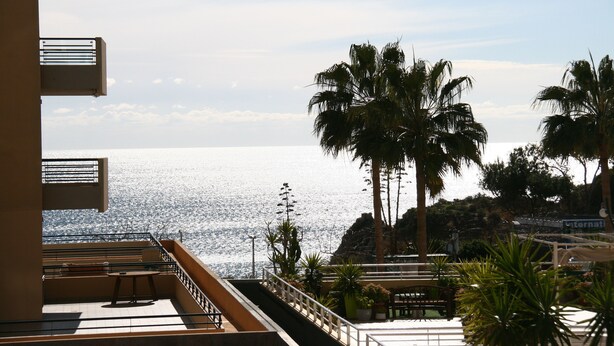 A balcony with a view of the sea, palm trees, and a building facade. - Apartment T2 Sea View - Varandas do Sol (Portimão)