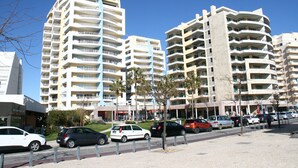 A multi-story residential building with balconies, a parking area with cars, and a clear blue sky. - Apartment T2 Sea View - Varandas do Sol (Portimão)