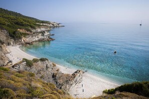 Une plage côtière aux eaux bleues et limpides, bordée de falaises rocheuses et d’un rivage sablonneux.