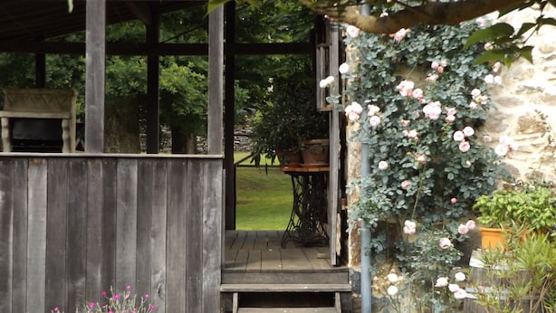 Une véranda en bois qui mène à un mur de pierre orné de rosiers grimpants.