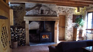 Une cheminée en pierre rustique avec un feu de bois, des poutres apparentes et un mur en pierre.