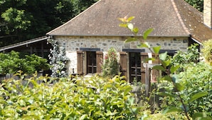 Un bâtiment en pierre avec un toit en pente, des volets en bois et un petit porche.