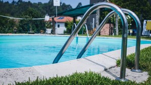 A swimming pool with metal pool ladders, a concrete edge, and a grassy area.