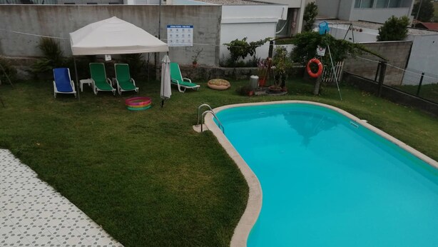 A swimming pool with a tiled deck, surrounded by green lawn and lounge chairs.