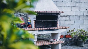 A concrete outdoor grill with a brick base, surrounded by a stone wall and potted plants.